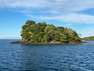Island with rocky shoreline and green trees surrounded by blue sea. Blue sea and clouds. Philippines.
