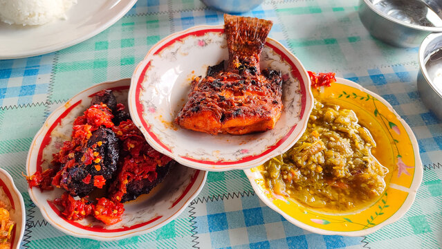 A plat of Spacy grill fish on a round plate. Another menu in the back. sajian makanan padang