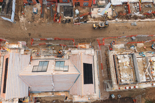Aerial view from drone at bustling construction site reveals various buildings under development, with workers and heavy machinery actively engaged in tasks