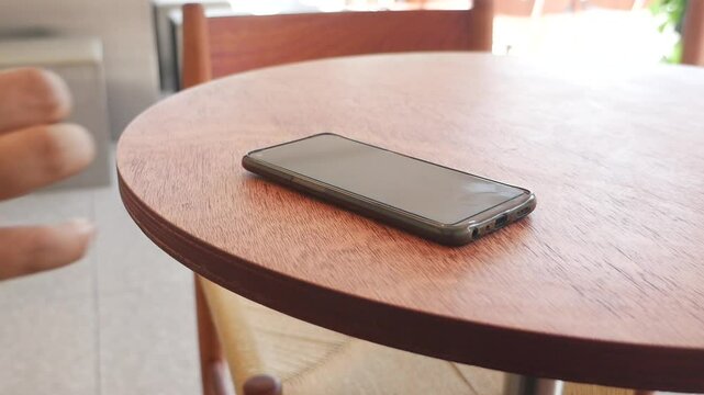 A hand grabbing and picking up mobile phone on the table.