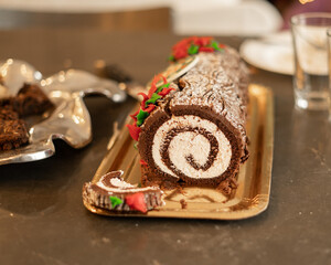 Chocolate yule log cake with cream filling on gold tray, surrounded by festive holiday table decorations