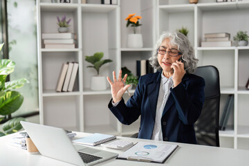 Elderly business woman expressing enthusiasm while on a phone call in a contemporary office
