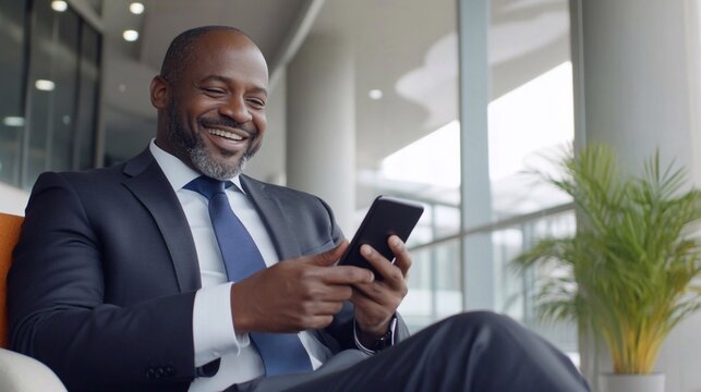 Busy happy african american professional business man sitting in office holding smartphone. Mature middle-aged businessman executive using ai apps on cellphone working at mobile phone at work.