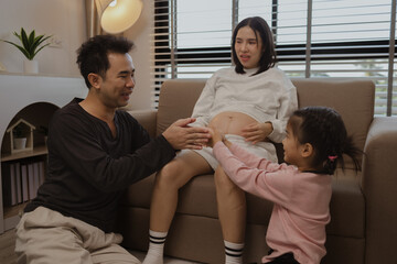 lovely family spend time together in their house, a pregnant mother sits on the couch with her husband and daughter enjoying a happy time together on a weekend