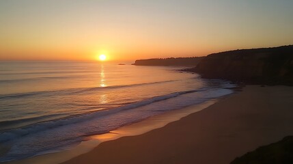 Fototapeta premium A breathtaking beach sunset with golden orange and pink hues in the sky, the sun setting just above the horizon and reflecting on the calm ocean