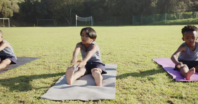 Stretching on yoga mats, children exercising outdoors during school PE class
