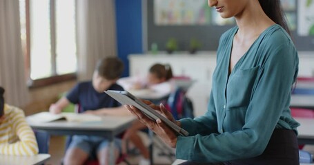 In school, teacher using tablet while students studying in classroom - Powered by Adobe