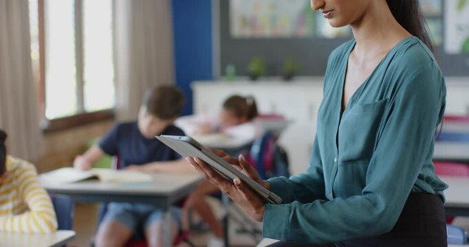 In school, teacher using tablet while students studying in classroom