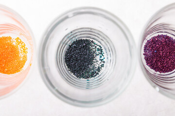 Transparent glasses on a white kitchen table in a line filled with a multi-colored paint of blue diluted food coloring prepared for coloring eggs before Easter.