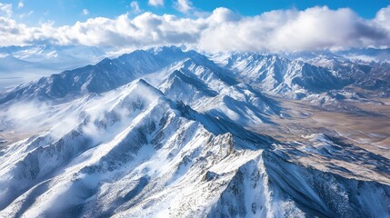 Vast mountain range under bright blue sky, snow-covered peaks with clouds, perfect for adventure and nature exploration.
