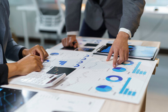 Business people analyzing financial charts and graphs using calculator in office