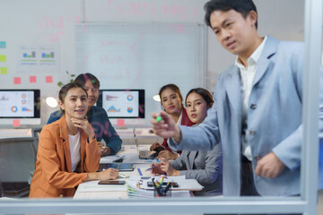 Asian manager writing on glass board explaining strategy to coworkers