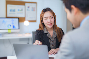 Obraz premium Asian businesswoman pointing at laptop explaining project to colleague in office meeting