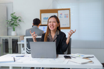 Stressed Asian businesswoman showing frustration while working with laptop in office