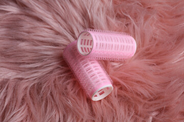 Plastic hair curlers on pink fuzzy background