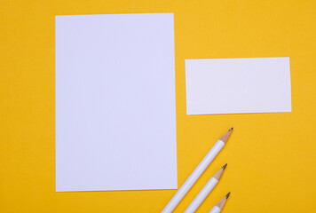 White blank card with paper sheet and pencils on yellow background