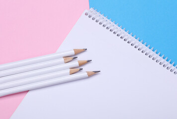 White wooden pencils and sketchbook on pink blue background. Mockup for design
