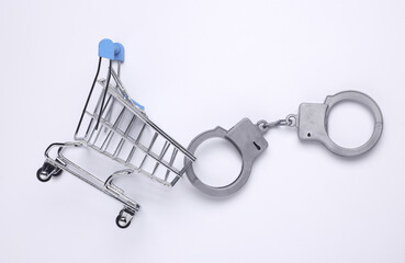 Miniature shopping cart with handcuffs on white background