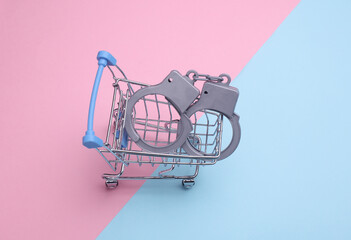 Miniature shopping cart with handcuffs on pink blue background