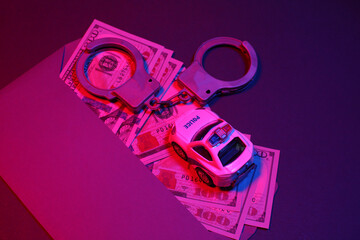 Envelope with hundred dollar bills and handcuffs, toy police car in red blue neon light. Justice,...