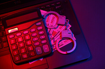 Laptop with handcuffs and dollar bills, calculator in neon light. Cyber ​​police