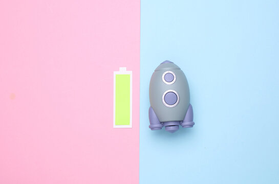 Toy space shuttle and Battery icon with full charge level on blue pink background. Startup idea