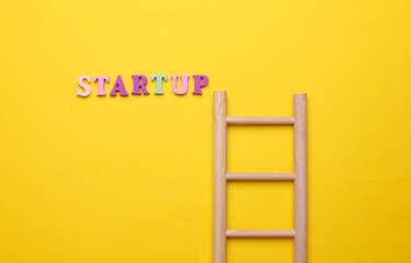 Wooden ladder and word startup on yellow background.
