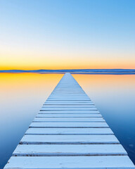 Obraz premium Wooden pier extending into calm lake at sunset, creating serene atmosphere