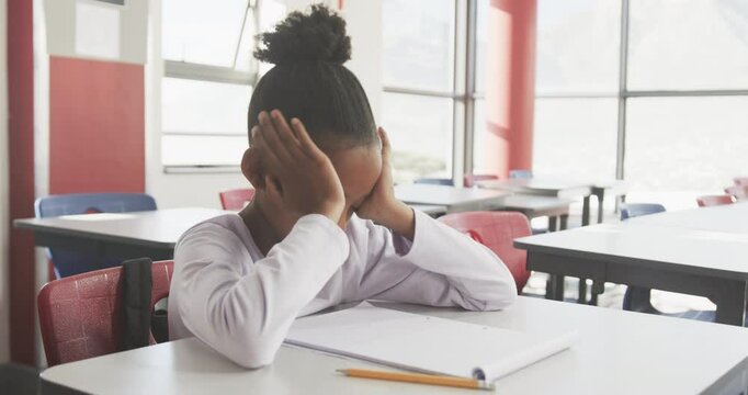 In school, African American girl sitting at desk with head in hands, feeling stressed