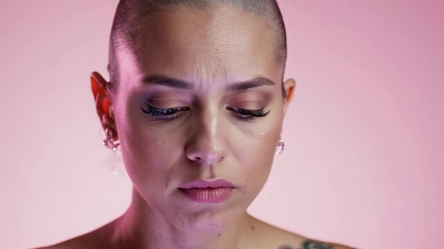 Static close-up video, soft diffused light, a woman with shaved head, delicate facial tattoos expressing wistful longing, monochrome pink background, soft gaze, faint sigh, sadness expression