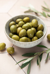 Green olives with olive branches resting in a bowl on a tiled surface