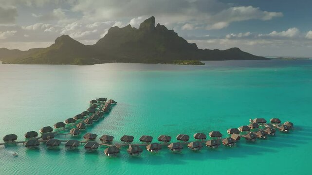 Stunning drone footage overwater bungalows lining a vibrant turquoise lagoon, mount Otemanu rising majestically in background, tropical paradise in Bora Bora. Travel exotic landscape vacation concept