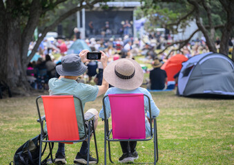 Couple taking photos using smartphone, unrecognizable crowds listen to the music concert in the...