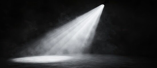 Bright spotlight beams down on a dimly lit stage creating a dramatic contrast against dark smoky shadows in the theater atmosphere