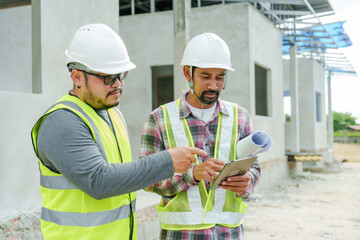 Architect and engineer wearing safety helmets and reflective vests reviewing construction plan on...