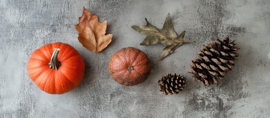Autumn flat lay with vibrant orange pumpkins, dried leaves, and pine cones arranged on a textured gray stone table with space for text