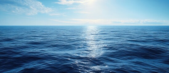 Obraz premium Aerial view of calm blue ocean waves under a bright sunny sky with soft clouds reflecting sunlight creating a tranquil and serene atmosphere