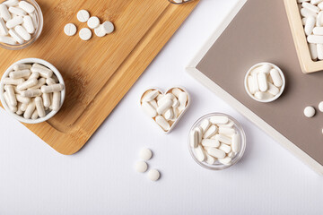 Different dietary supplement pills, minerals and vitamins such as such as vitamin d3, a, e, b, c, magnesium, zinc and calcium in beautiful composition from above on a wooden desk on white background.