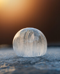 Close up of frozen soap bubble on snow with warm light behind it.