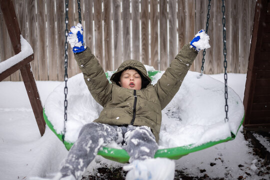 Child in winter clothes playing on a snow-covered swing outdoors