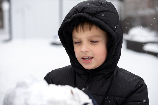 Young boy in winter coat holding a snowball in a snowy backyard