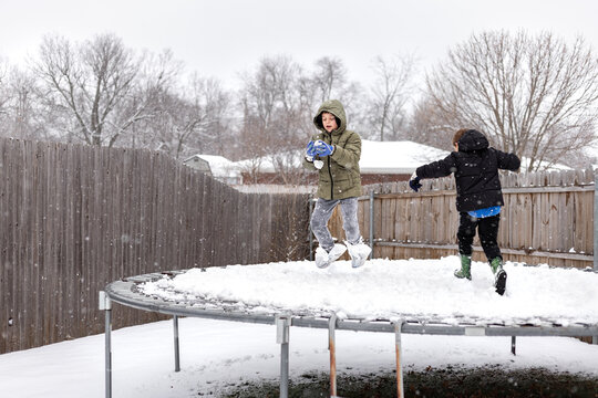 Two kids play in the snow on a backyard trampoline in winter