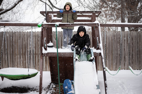 Two kids playing on snow covered slide and playset