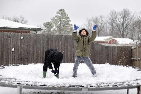 boy throwing snow in air on trampoline during winter storm
