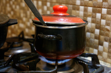 A black pot with a red lid sits on a stove burner