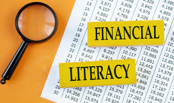 FINANCIAL LITERACY - words on yellow wooden blocks on the background of a magnifying glass and a table with numbers