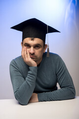 A young man in a graduation cap and casual sweater sits thoughtfully at a desk, symbolizing the blend of academic achievement and personal reflection. Perfect for educational and inspirational themes.