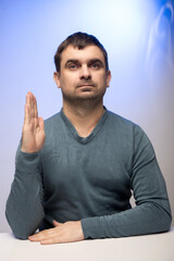 A person in a teal sweater raises their right hand, possibly taking an oath or making a pledge. The...