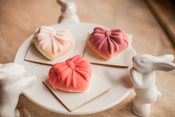 A close-up of a  plate featuring artistic heart-shaped mousse cakes in soft pink hues, decorated with bows. Delicate golden 