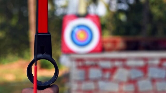 Young Indian man practicing archery in a park, focusing on his target in a natural outdoor setting.